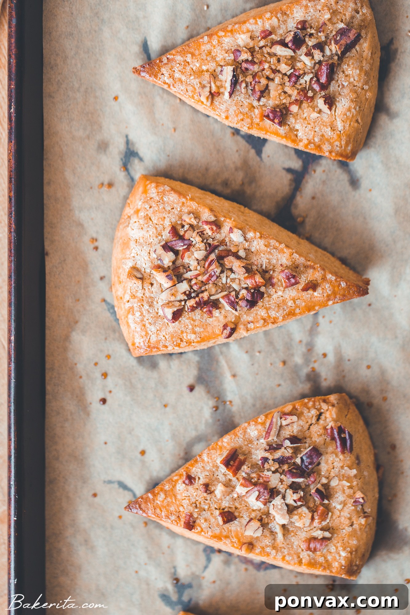 A stack of golden brown Gluten-Free Vegan Pumpkin Scones, glistening with maple glaze and sprinkled with chopped pecans, on a rustic wooden board.
