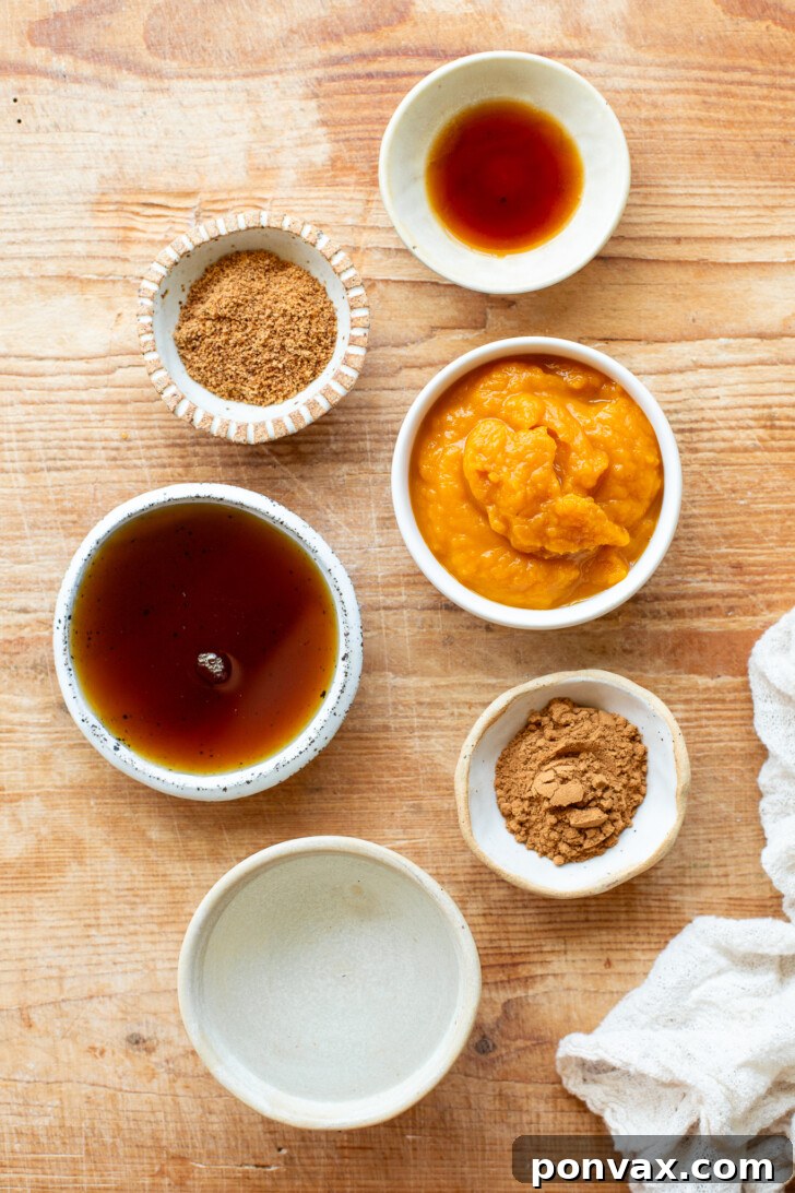 Ingredients for pumpkin spice syrup in bowls: coconut sugar, vanilla extract, maple syrup, pumpkin puree, water, and pumpkin pie spice on a wooden bread board.