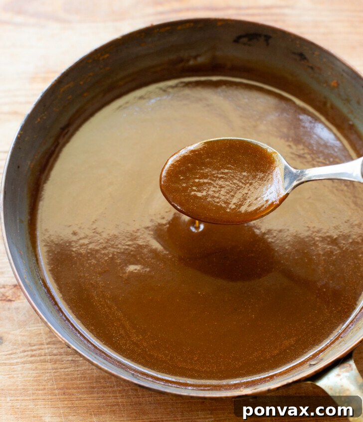 Freshly made pumpkin spice syrup being poured into a glass bottle.