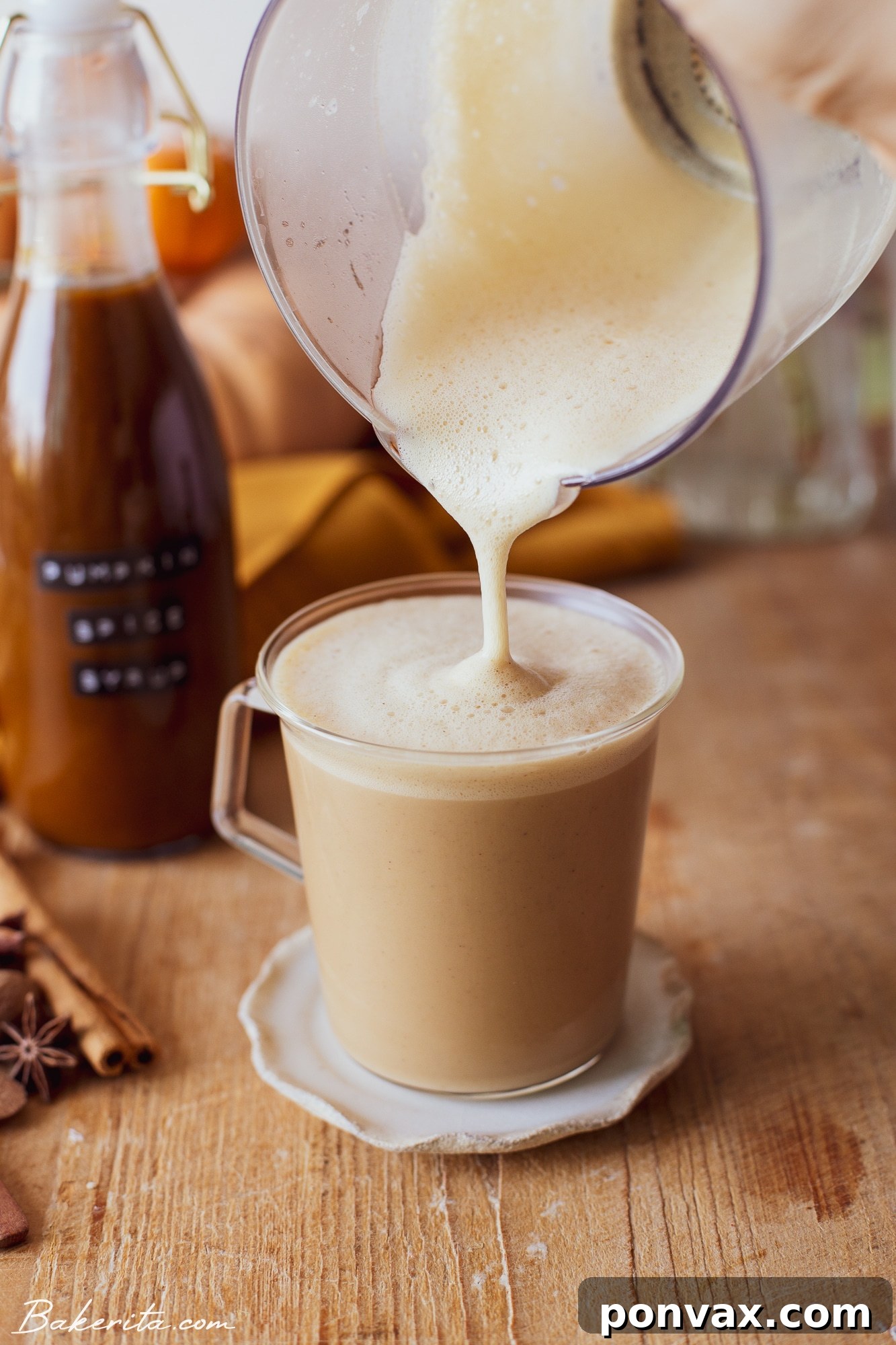 A close-up of a glass of pumpkin spice latte with whipped cream and cinnamon stick.