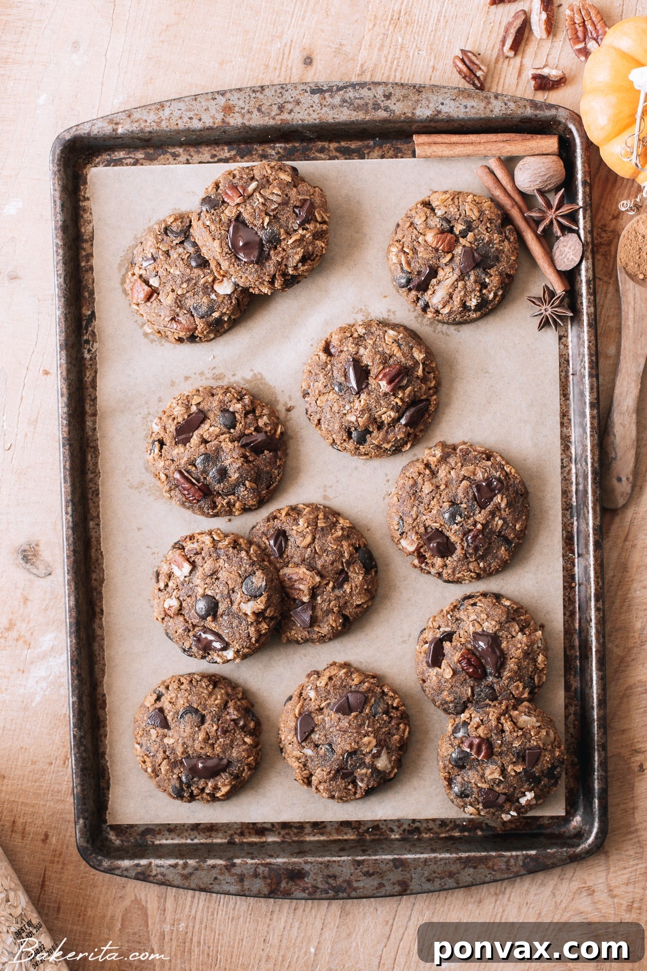 Plant-Based Pumpkin Spice Oat Delights 6 A close-up of a rustic wooden surface adorned with baked pumpkin oatmeal cookies, scattered chocolate chips, and whole pecans.