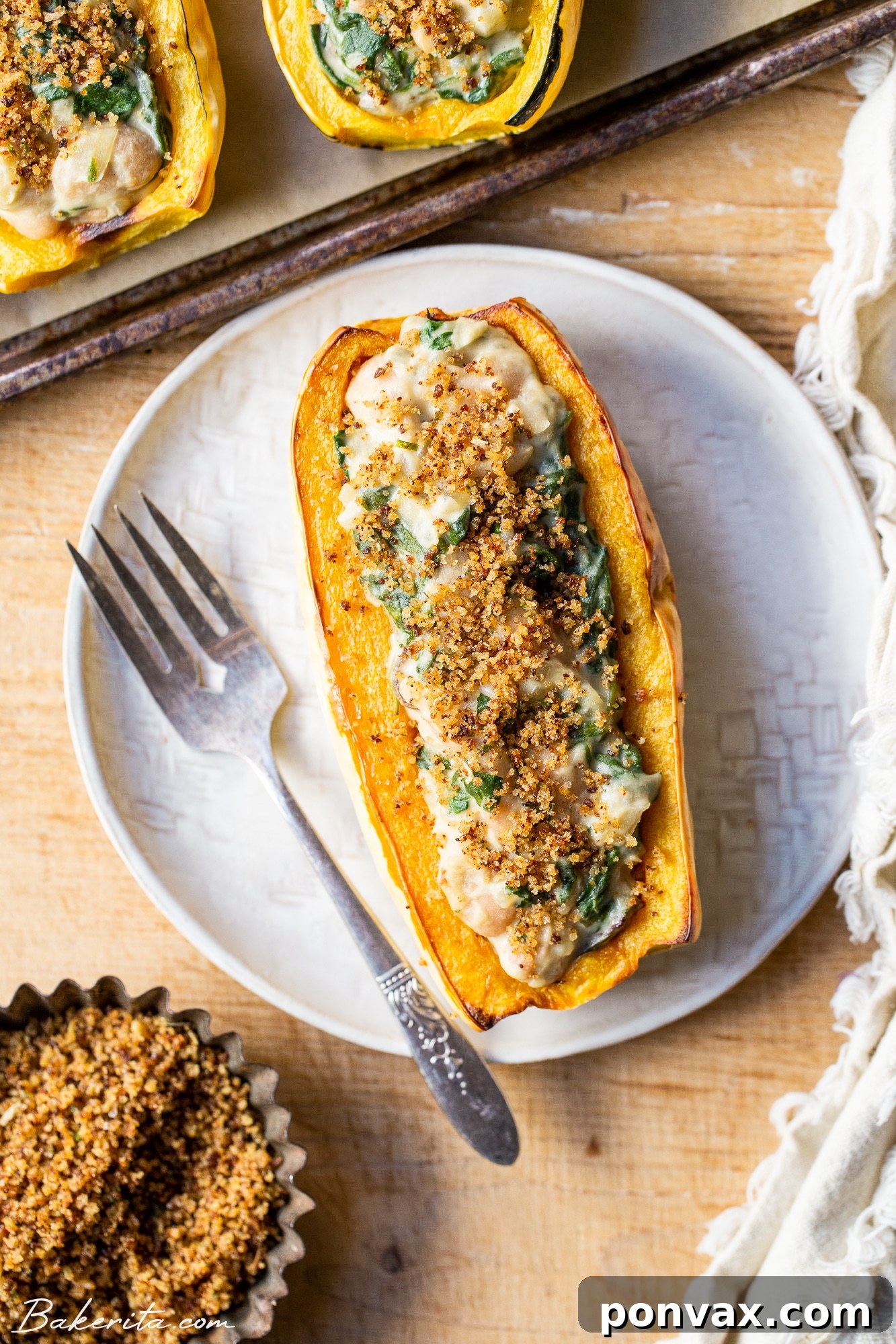 Two halves of Vegan Creamed Spinach & White Bean Stuffed Delicata Squash on a plate, garnished with fresh herbs.