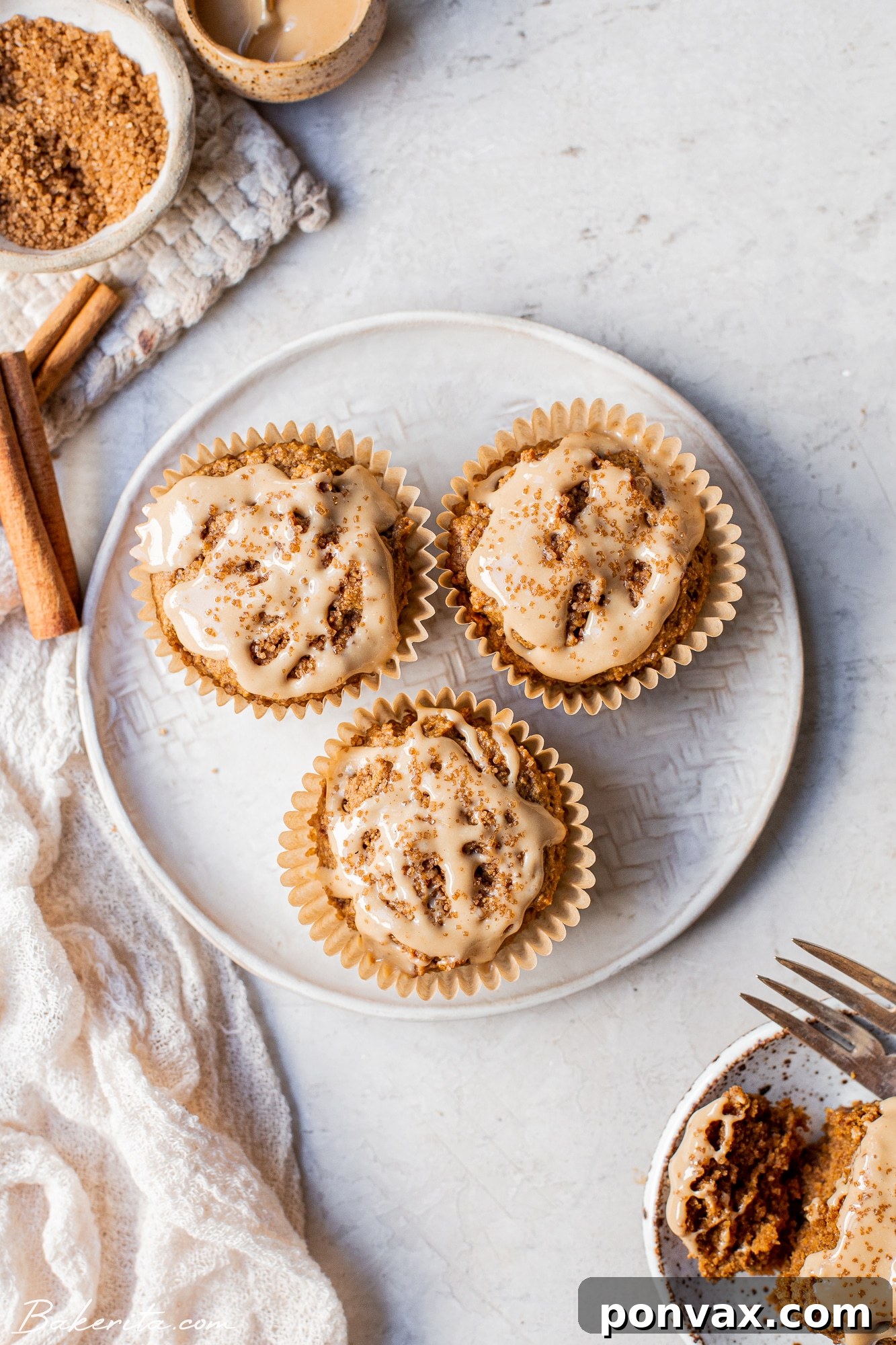 A close-up shot of two Gluten-Free Vegan Chai Muffins with a simple cashew butter glaze and crunchy sugared tops, sitting on a wooden board.