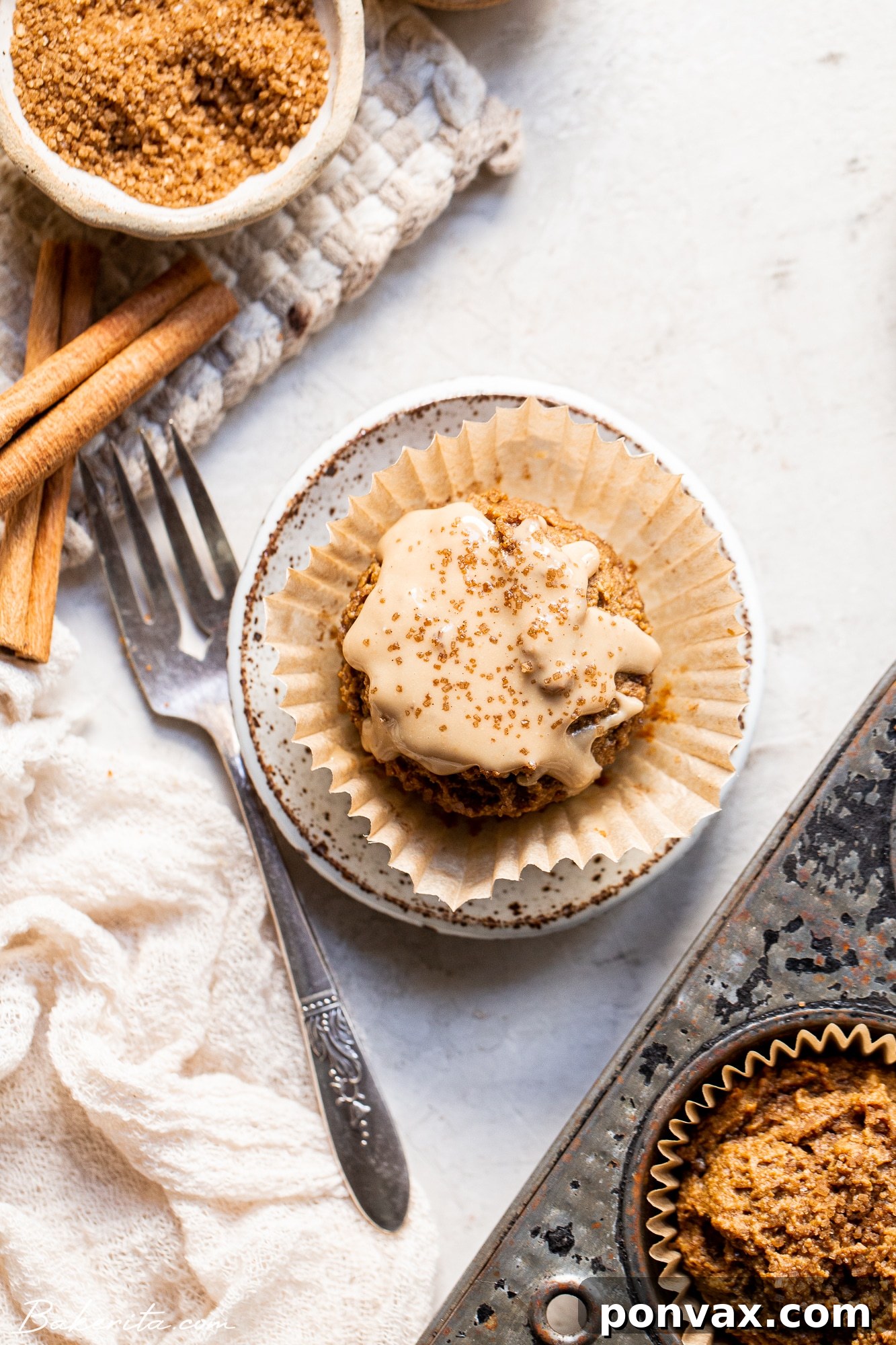 A beautifully glazed Gluten-Free Vegan Chai Muffin with a bite taken out, revealing its soft interior, placed on a white plate with tea.