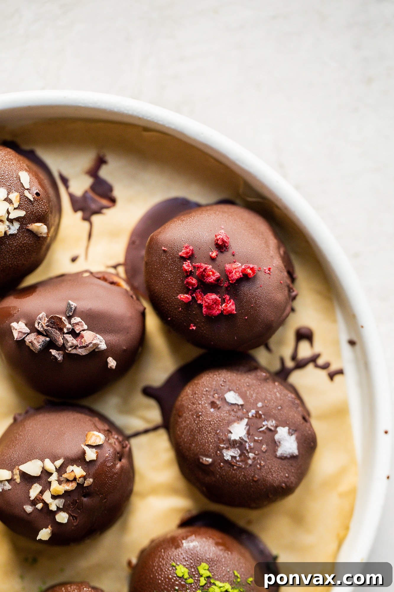 Three chocolate-covered Daily Harvest bites, each with a unique topping, arranged on a rustic plate.