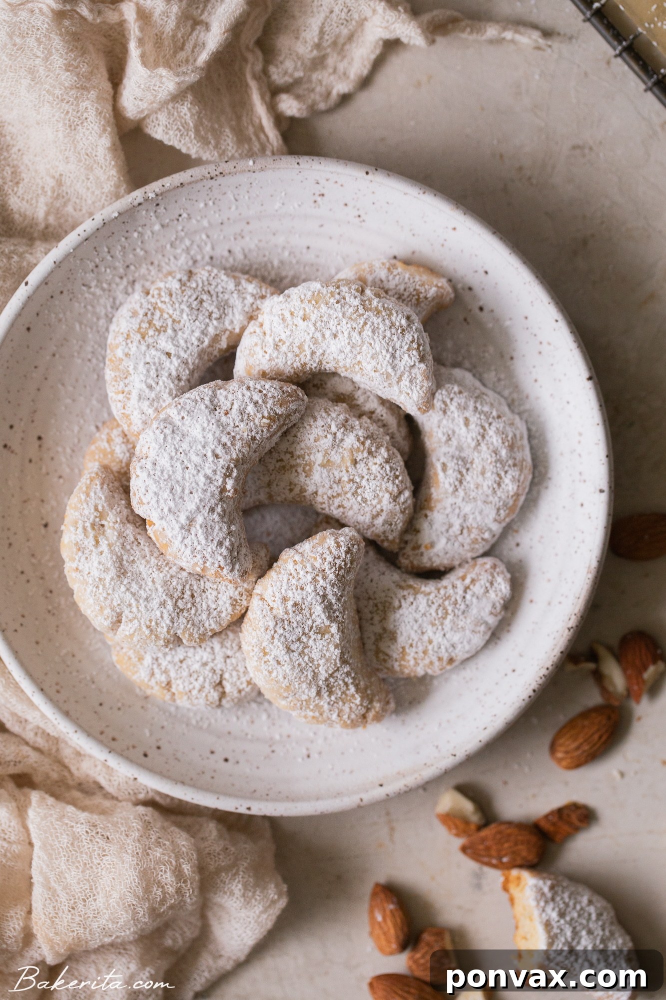 Crispy Vegan Almond Crescent Cookies dusted with powdered sugar, served on a white plate with coffee.