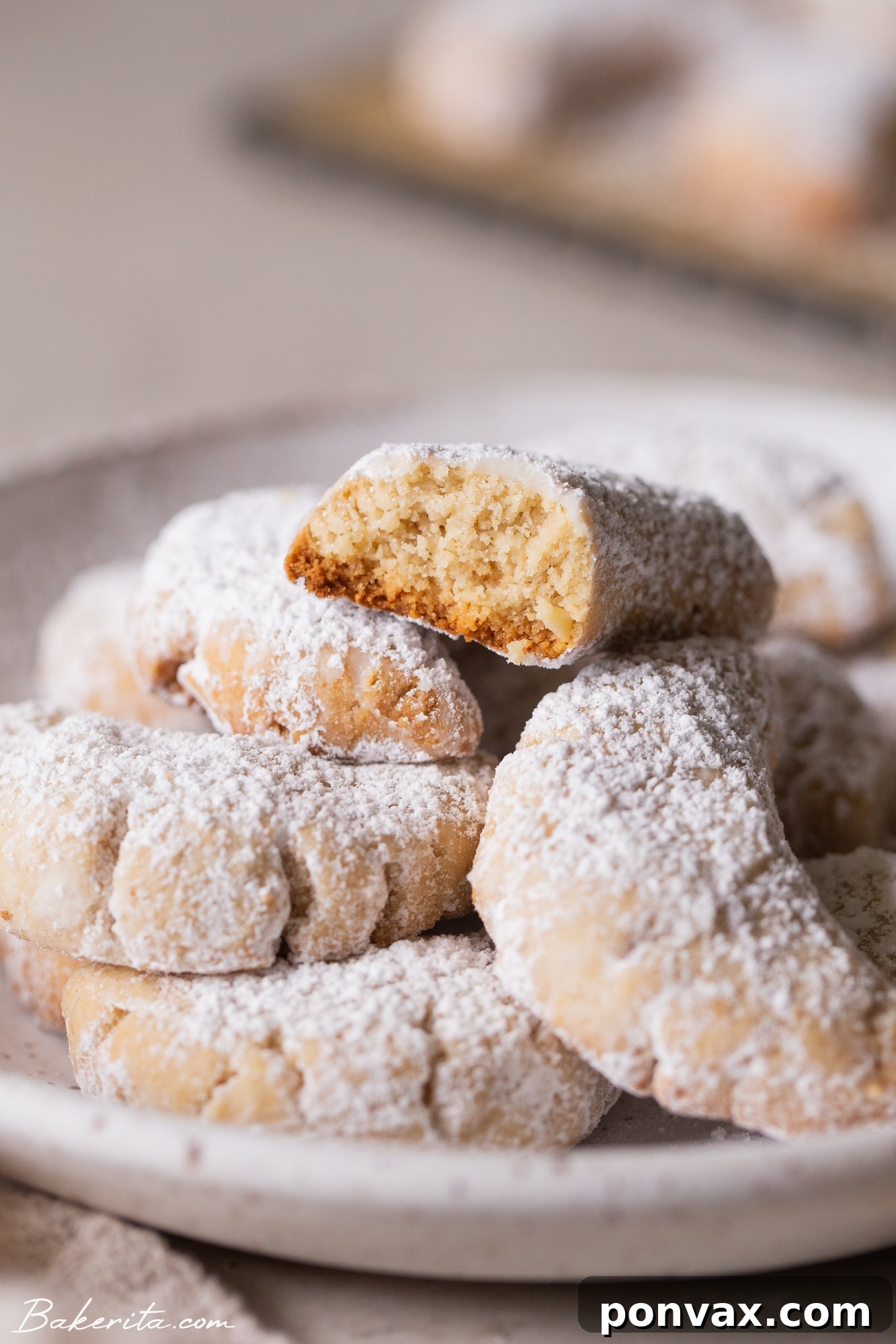 Freshly baked Vegan Almond Crescent Cookies on a baking sheet, golden brown and ready for powdered sugar.