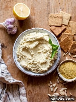 Velvety 5-Minute Vegan Almond Ricotta 7 A beautifully presented bowl of creamy vegan ricotta, garnished with fresh basil leaves, next to a crisp cracker spread with the plant-based cheese.