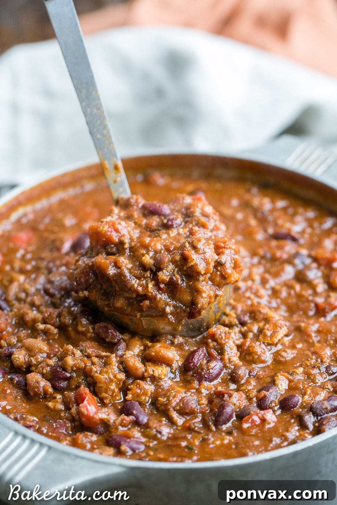 A close-up of a rustic spoon scooping up a generous portion of My Best Chili, highlighting the rich tomato base, mixed beans, and savory meats.