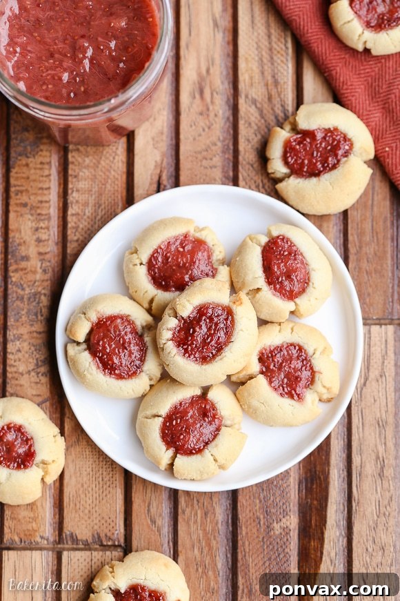Simple & Sweet: Gluten-Free Vegan Jam Thumbprint Cookies 4 A white plate showcasing Gluten-free and vegan Thumbprint Cookies with strawberry rhubarb chia jam, set against a rustic wooden background with a jar of jam subtly blurred in the background.