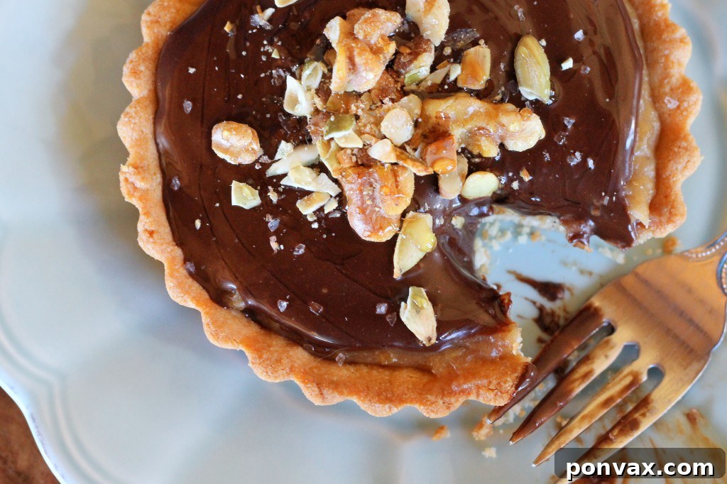Close-up of a mini Chocolate Date Caramel Tart, featuring a rich date caramel layer and chocolate ganache, sprinkled with walnuts and sea salt. It's a perfect paleo, gluten-free, and vegan treat. #vegantart #glutenfree #paleodessert #tartrecipe