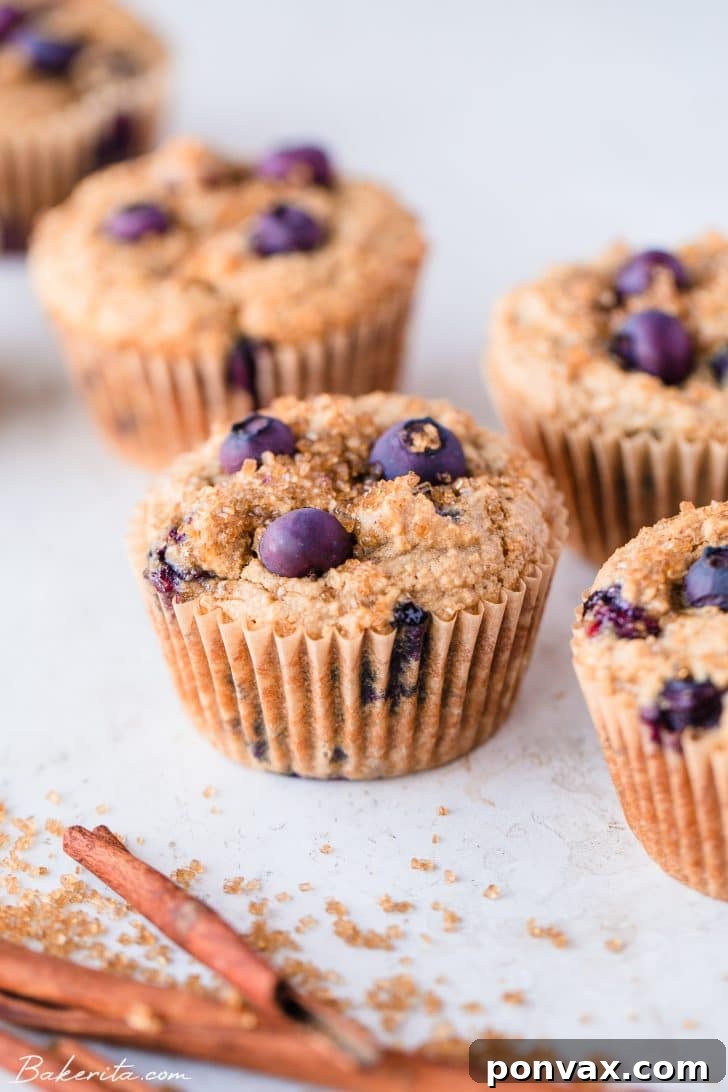 A neat row of five vegan and gluten-free blueberry muffins, each in its parchment liner, set against a pristine white background.