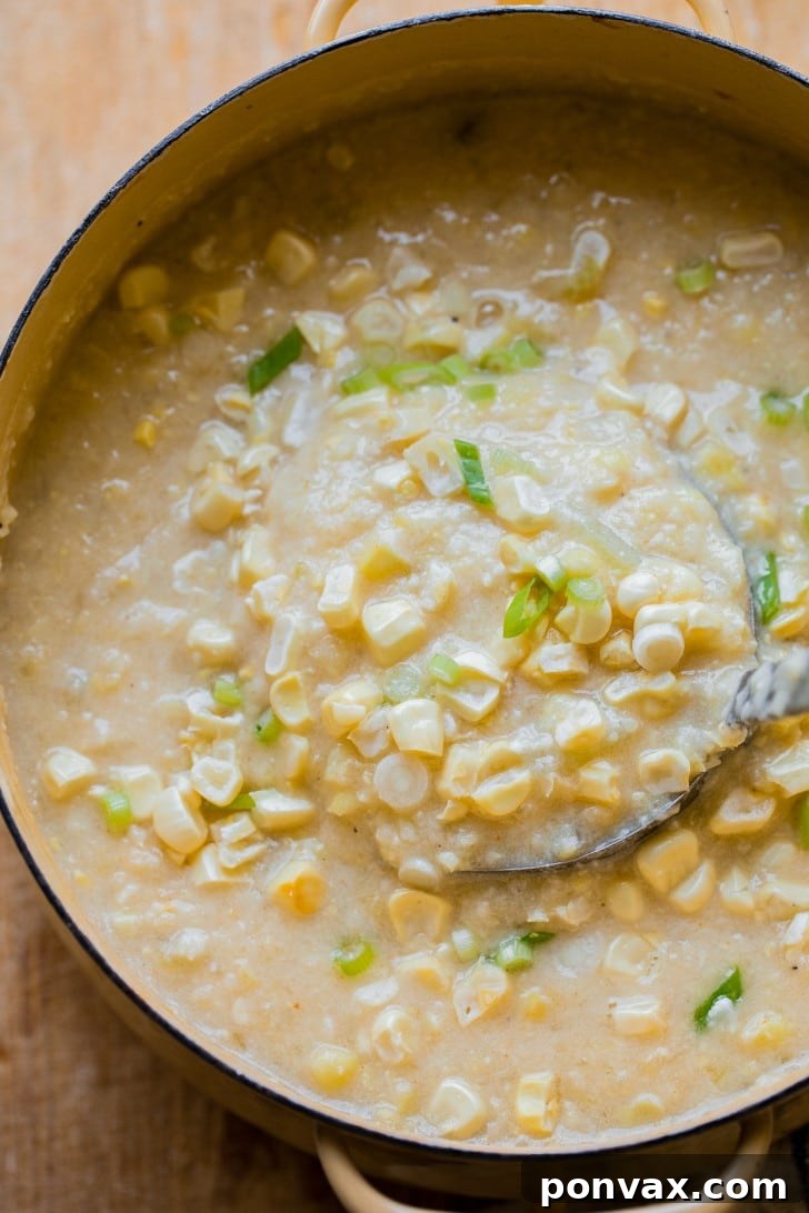 Golden Vegan Corn Chowder 5 A pot full of vegan corn chowder being ladled out, garnished with fresh sweet corn kernels and green onions.