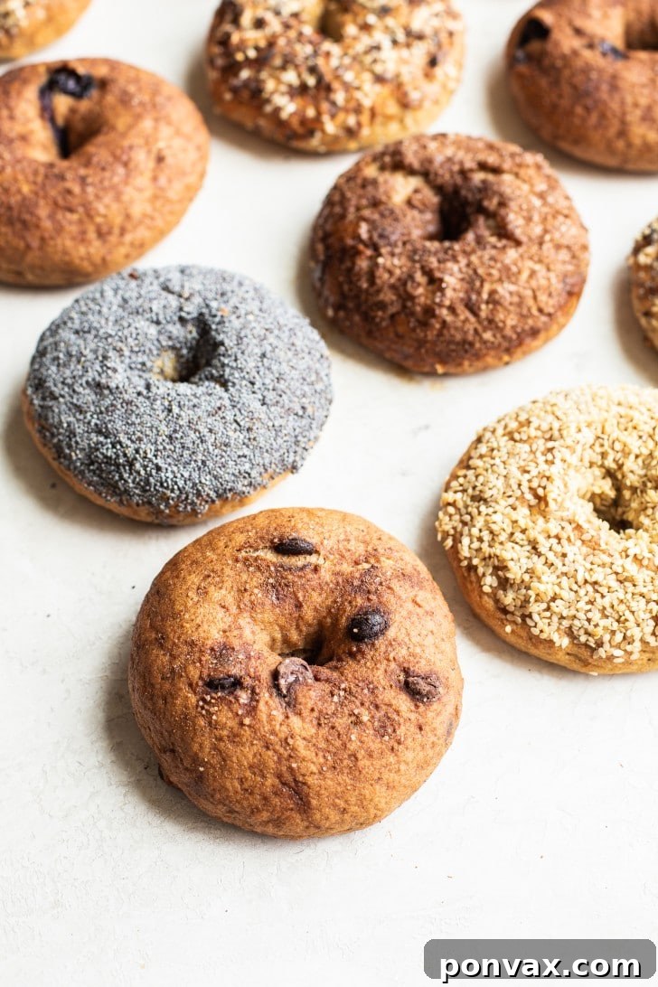 A stack of freshly baked gluten-free bagels on a cooling rack, some topped with seeds.