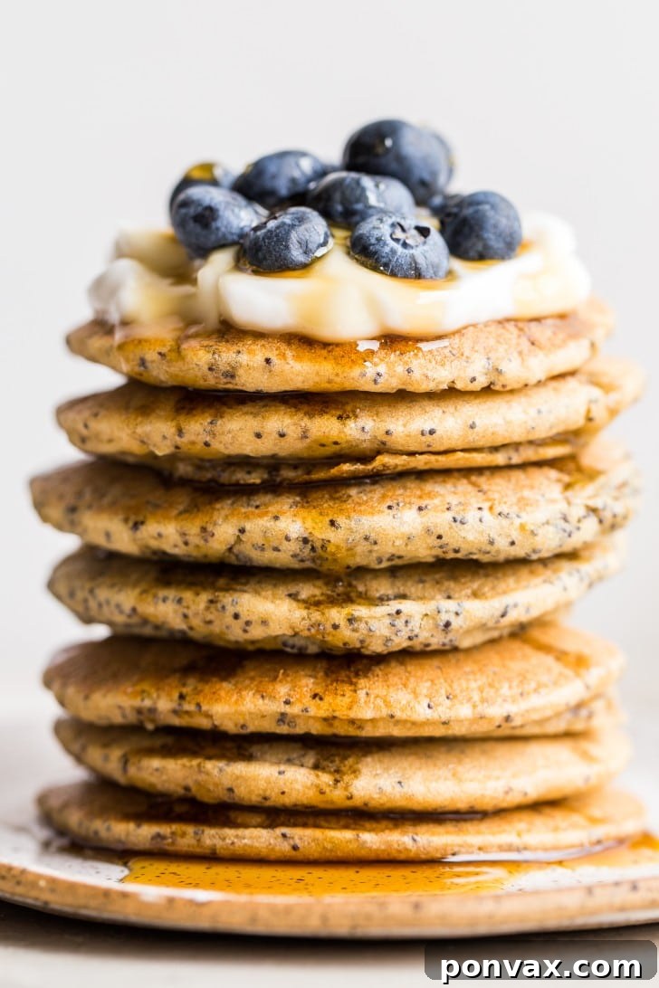 A close-up shot of a stack of golden brown Vegan Lemon Poppyseed Pancakes garnished with fresh lemon zest.
