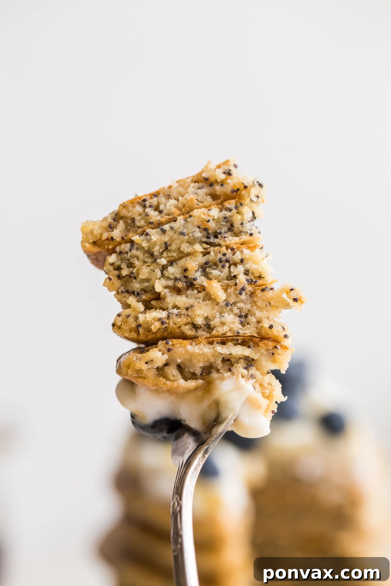A stack of golden brown Vegan Lemon Poppyseed Pancakes on a white plate with a side of berries.