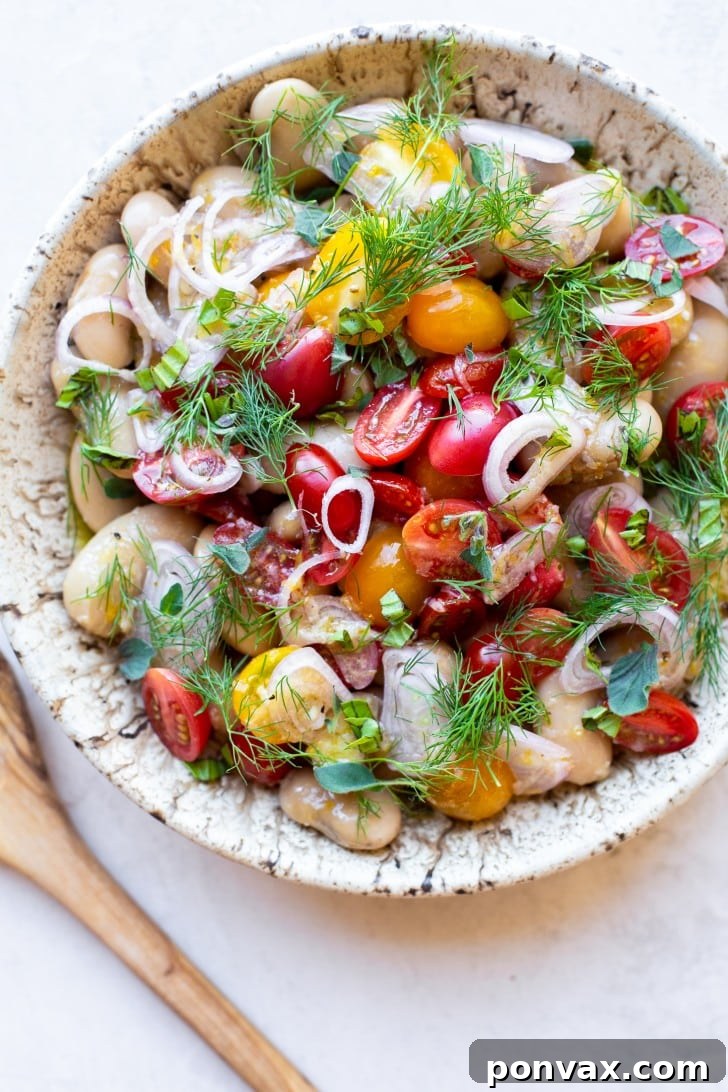 A close-up shot of the Herby Marinated White Bean Salad, showcasing the giant white beans, halved cherry tomatoes, and green herbs in a glass bowl.