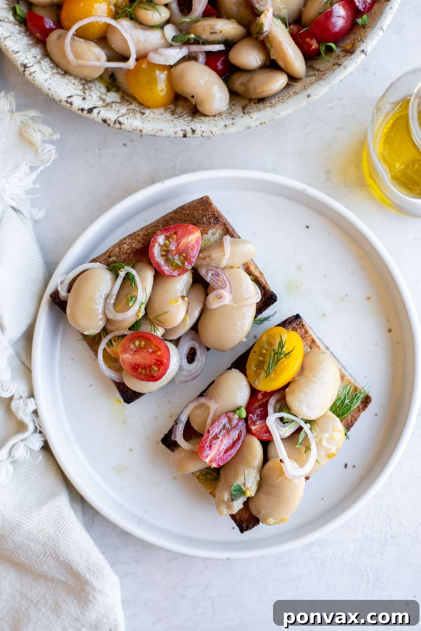 A rustic shot of a bowl of Herby Marinated White Bean Salad with a wooden spoon and a sprig of fresh herb.
