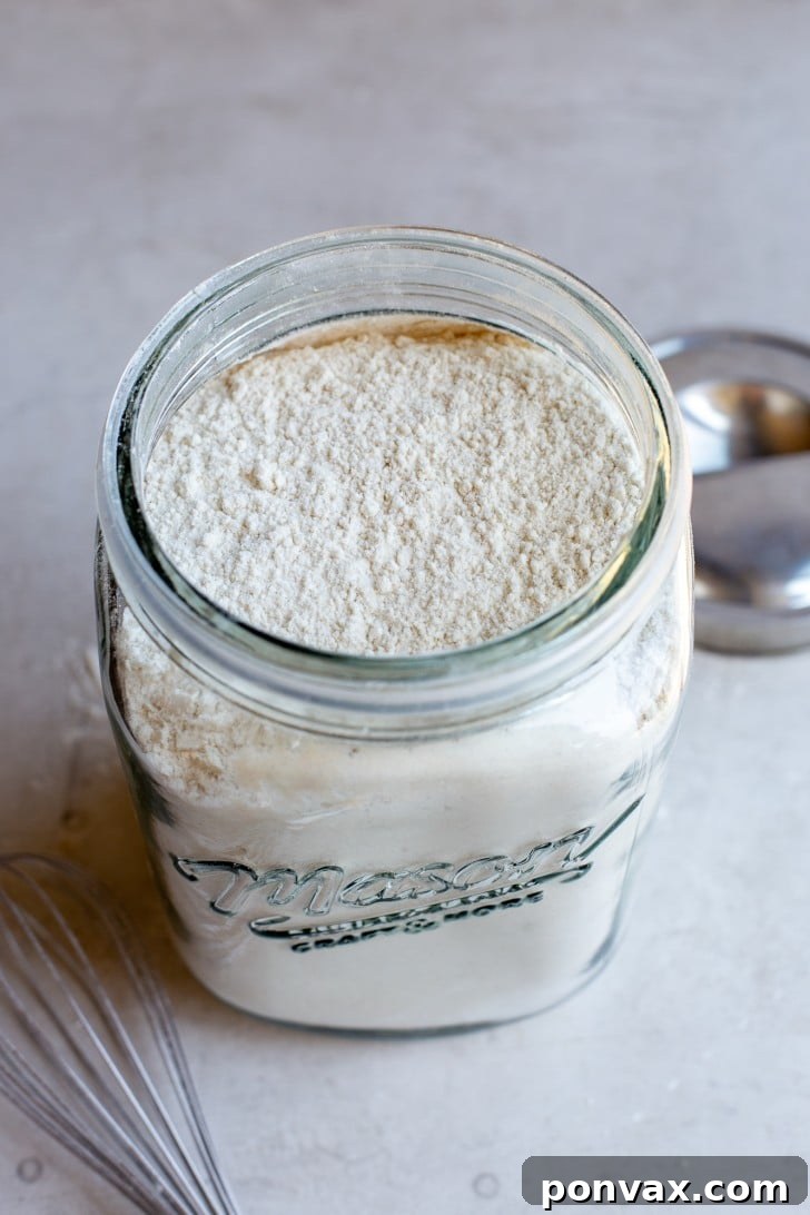 An overhead shot of a large mason jar filled with the Gluten-Free Bread Flour Blend, with a whisk resting casually in the foreground, highlighting the ease of preparation.