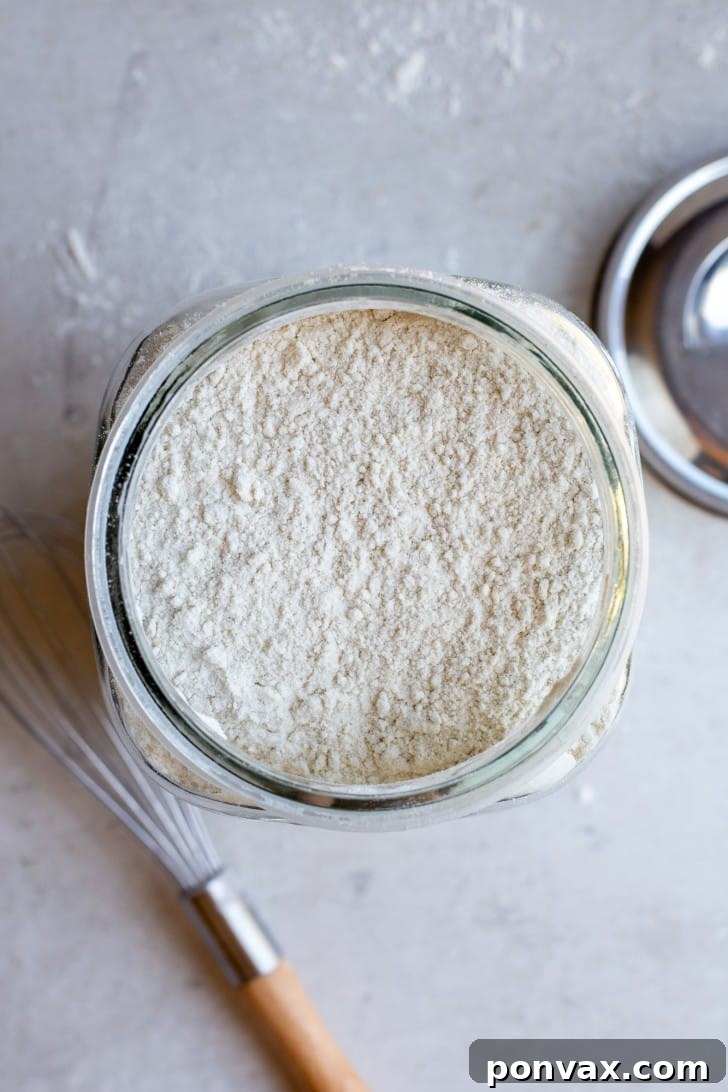 An inviting overhead view of the Gluten-Free Bread Flour Blend in a large mason jar, with a silver lid and a whisk in the background, signaling freshness and homemade goodness.
