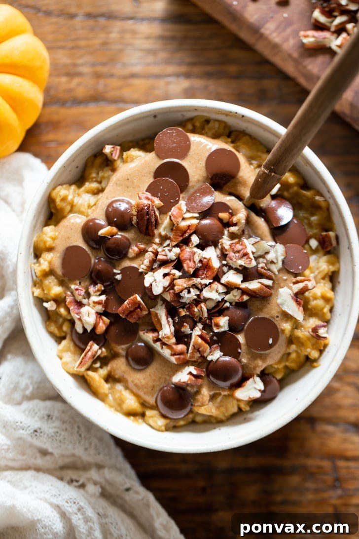 Creamy Easy Pumpkin Oatmeal topped with chocolate chips, granola butter, and pecans in a white bowl, ready to be enjoyed.