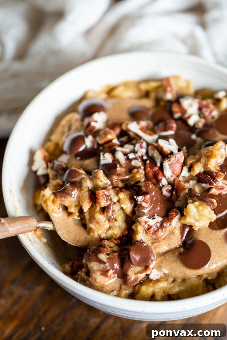 A close-up of a beautifully topped Easy Pumpkin Oatmeal bowl, showcasing melted chocolate chips, granola butter, and crunchy pecans, ready for a spoonful.