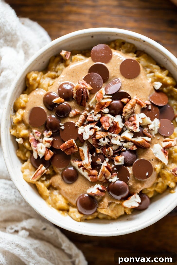 A top-down view of a spoonful of creamy Easy Pumpkin Oatmeal being lifted from the bowl, showing its rich texture and delicious toppings.