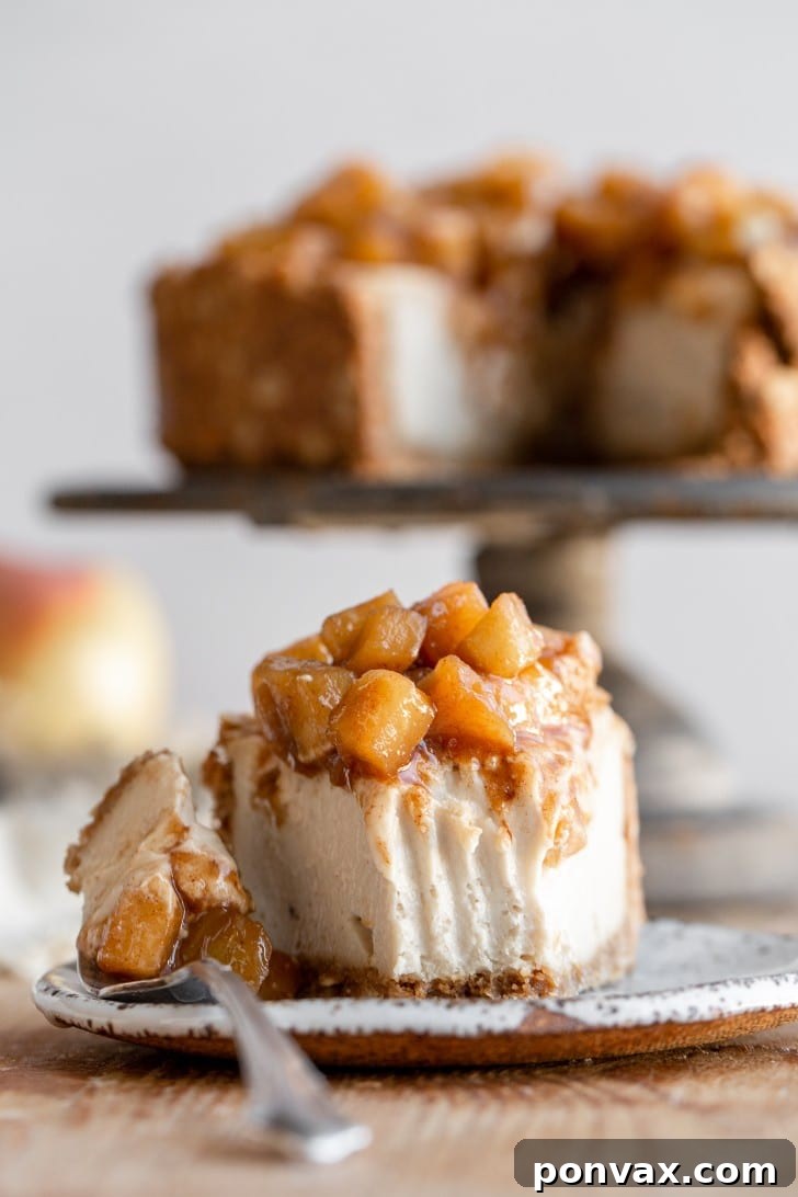 A fork taking a bite out of a glorious slice of vegan apple cheesecake, highlighting its creamy filling and perfectly cooked apple topping. The remainder of the whole cheesecake rests elegantly on a cake stand in the soft-focused background, beckoning for more.