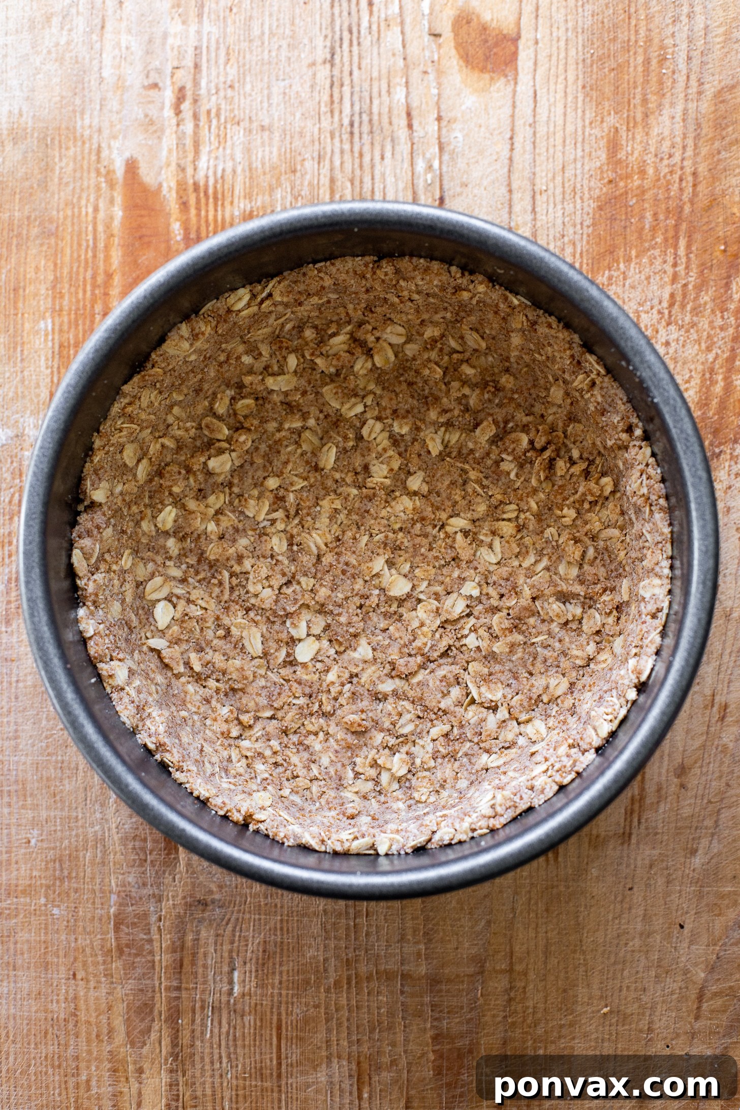 A chef's hands pressing the gluten-free oatmeal almond flour crust mixture evenly into an 8-inch springform pan, preparing it for baking. This step ensures a firm and delicious base for the vegan cheesecake.
