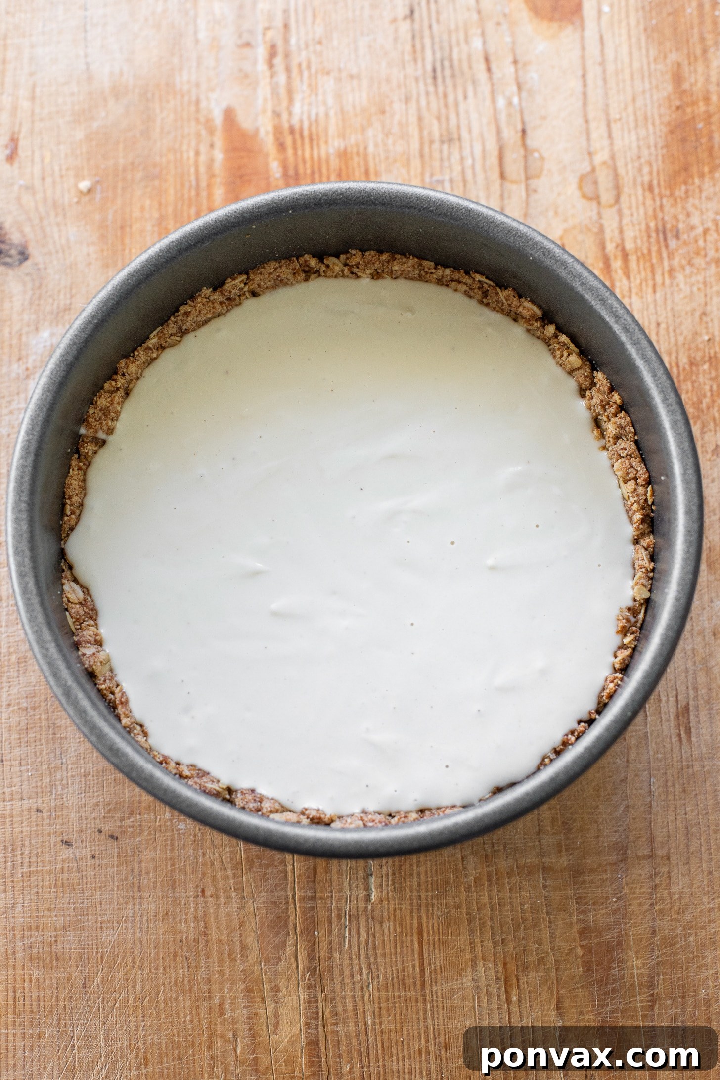 The vegan apple cheesecake, freshly baked and golden, cooling on a wire rack. The edges show the perfectly set crust, and the center is ready to receive its luscious apple topping.