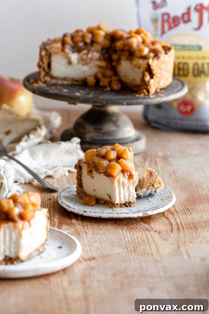 The finished Vegan Apple Cheesecake, with its golden-baked crust and creamy filling, topped generously with a luscious, spiced apple pie mixture. The dessert is cooling, ready to be chilled and served.