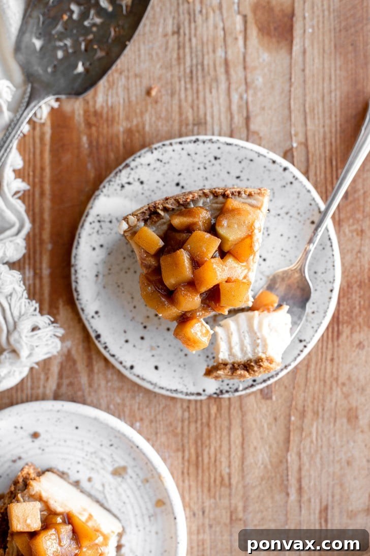 An overhead shot of a delightful slice of vegan apple pie cheesecake, with a fork bite removed, artfully placed on a wooden board. A vintage cake server rests elegantly beside it, suggesting a moment of shared indulgence.
