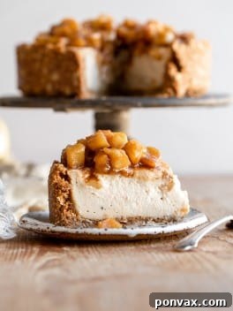A delicious slice of vegan apple cheesecake with a golden crust and creamy filling, topped with a generous layer of spiced apple pie filling. The full cheesecake is in the background.