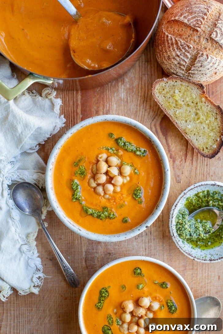 Sun Kissed Roasted Tomato and Chickpea Comfort 2 A vibrant bowl of roasted tomato chickpea soup, garnished with fresh herbs and a swirl of pesto, served on a wooden surface.