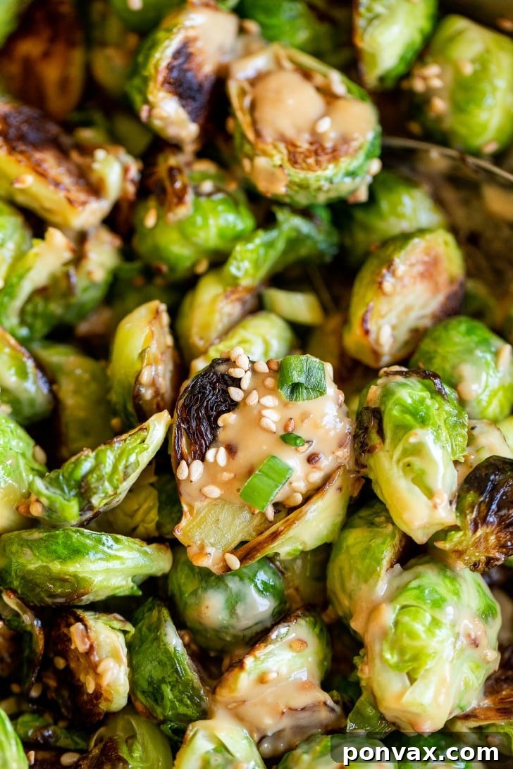 Glazed Miso Sesame Brussels Sprouts 6 A bowl of Miso Sesame Brussels Sprouts with a serving spoon, beautifully garnished with green onions and sesame seeds, ready to be enjoyed.