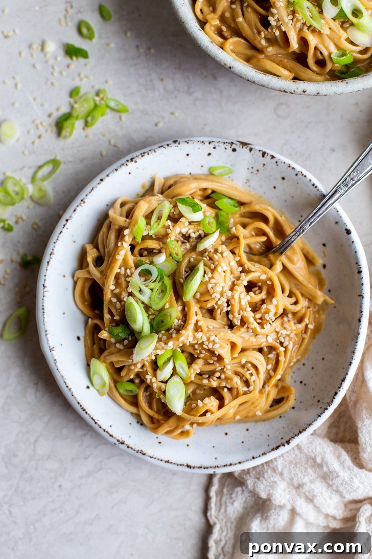 Velvety Peanut Noodles in 5 Minutes 2 A bowl of creamy peanut noodles, garnished with green onions and sesame seeds.