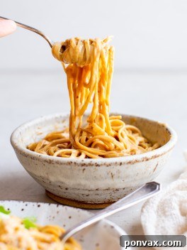 A bowl of creamy peanut noodles, garnished with green onions and sesame seeds.