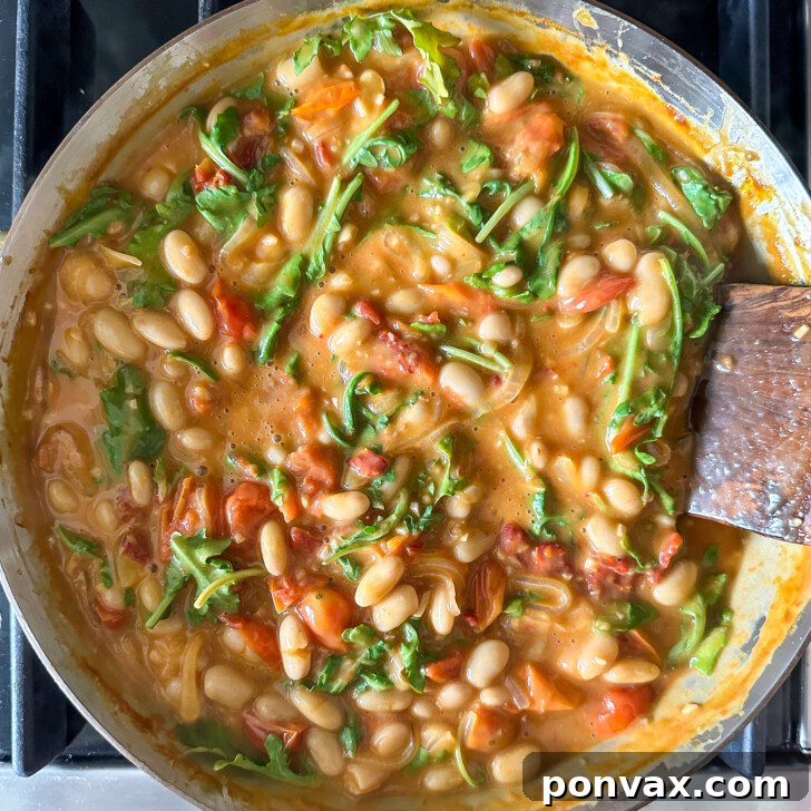 Velvety Tomato and Cannellini Stew 12 Vegan cream cheese and greens being stirred into the stew.
