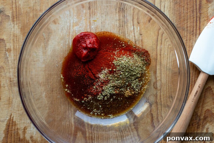 Tomato paste, apple cider vinegar, tamari, and spices mixed in a bowl, forming a paste.