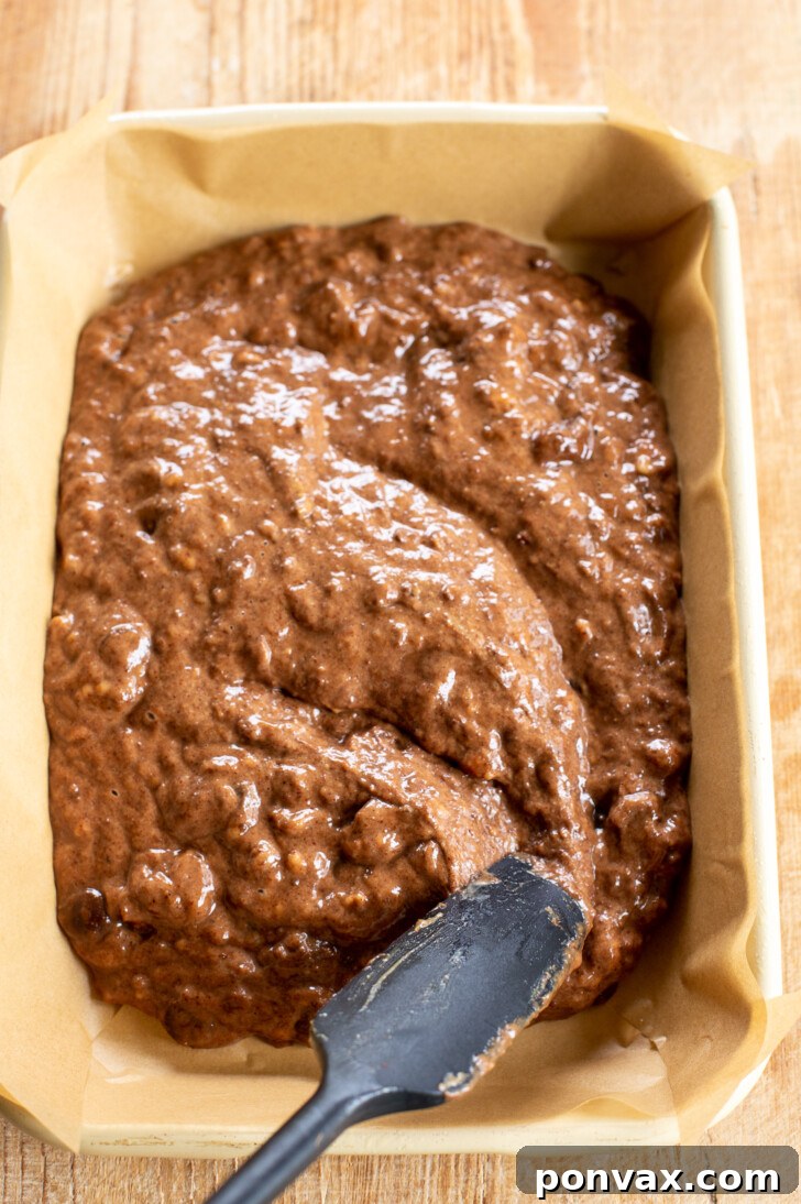Pouring brownie batter into a parchment-lined baking dish.