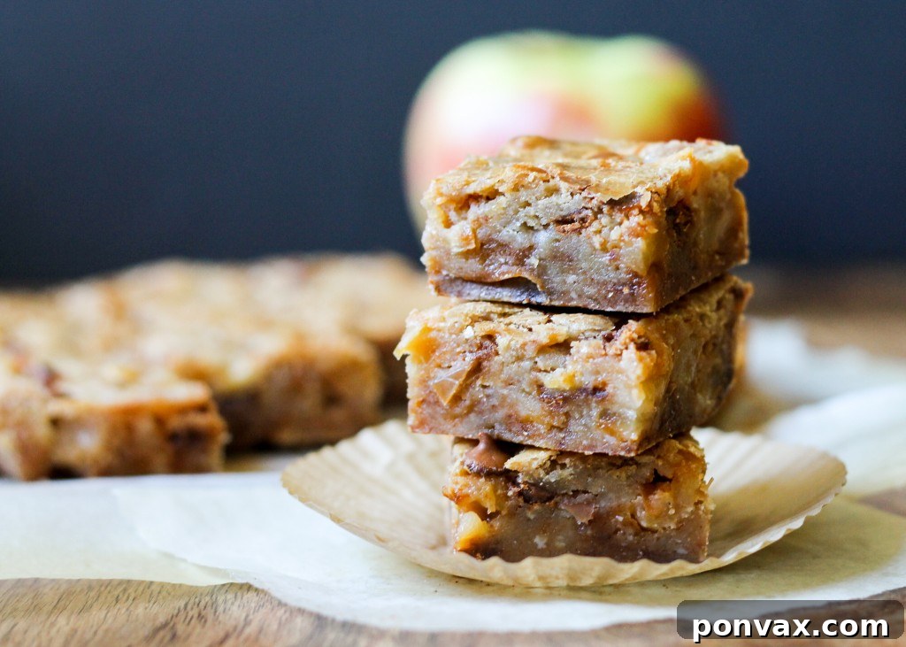 Golden-brown Apple Cinnamon Blondies cooling on a rack, garnished with fresh apple slices and cinnamon sticks, highlighting their rich texture.