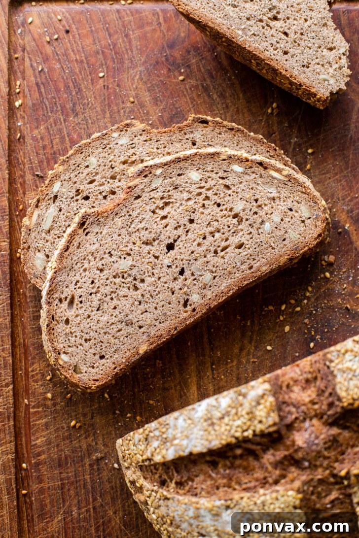 A slice of hearty Gluten-Free Rye Bread on a wooden board, showcasing its rich brown color and caraway seeds.