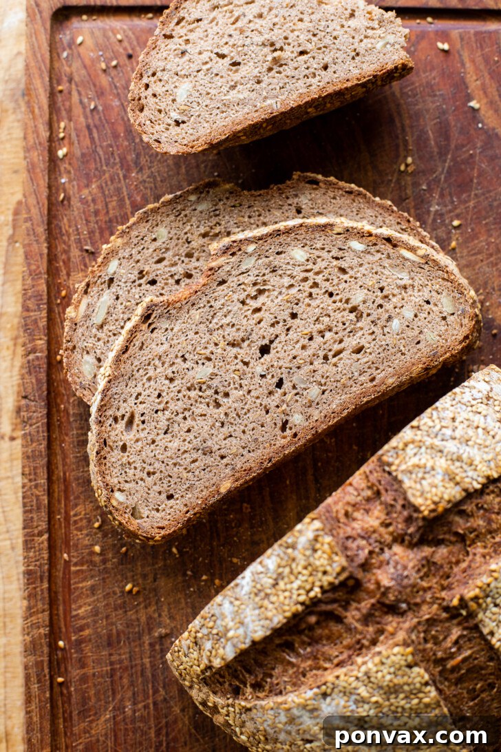 Two slices of Gluten-Free Rye Bread, one plain and one with avocado, on a cutting board next to a full loaf.