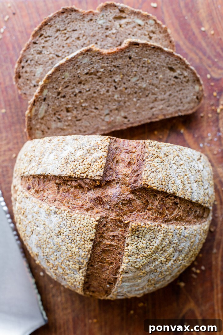 Two hands holding a freshly baked loaf of round Gluten-Free Rye Bread, with a rustic, dark crust.