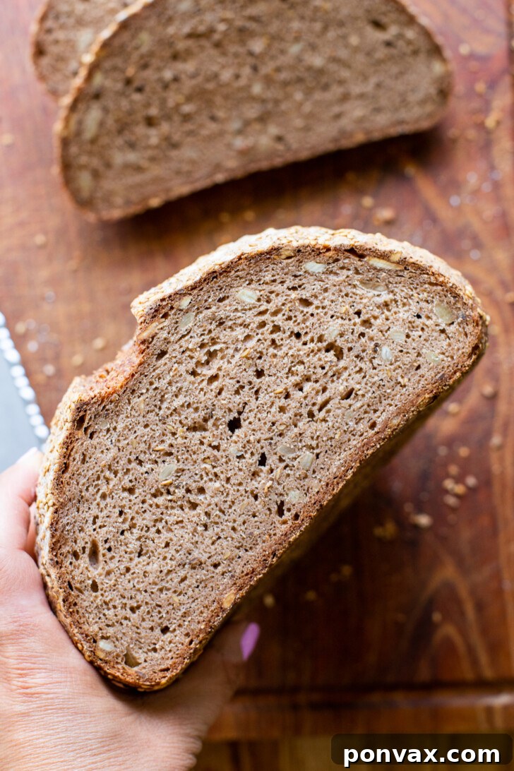 A close-up of Gluten-Free Rye Bread dough in a mixing bowl, showcasing its dark color and visible caraway seeds.