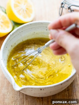 A small jar of homemade lemon vinaigrette with a wooden spoon, ready to be served, showcasing its vibrant color and fresh ingredients.