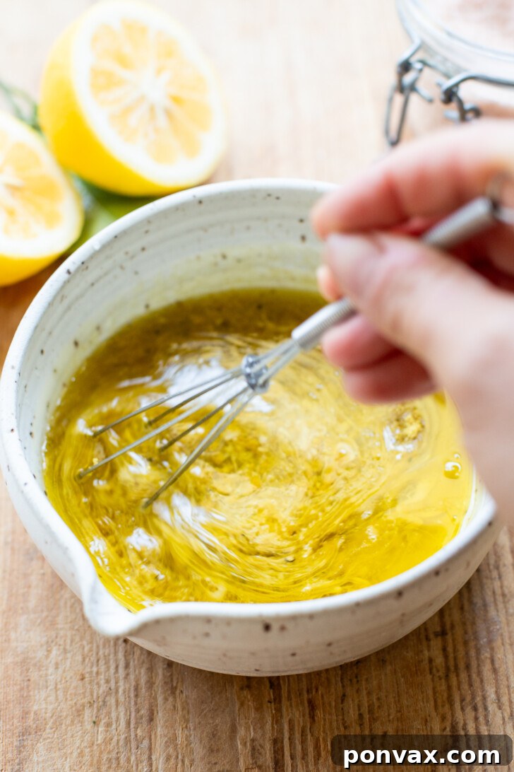 A close-up of the finished lemon vinaigrette in a small bowl, garnished with fresh herbs and lemon slices, ready to serve.