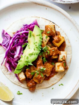 Flavor-Packed Sriracha Tofu Tacos 8 One Sriracha Tofu Taco on a ceramic plate, topped with avocado, red cabbage, salsa, and cilantro.