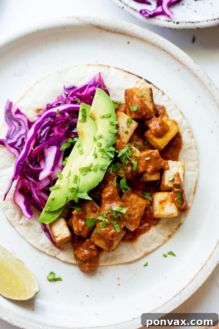 Flavor-Packed Sriracha Tofu Tacos 3 One Sriracha Tofu Taco on a ceramic plate, topped with avocado, red cabbage, salsa, and cilantro.