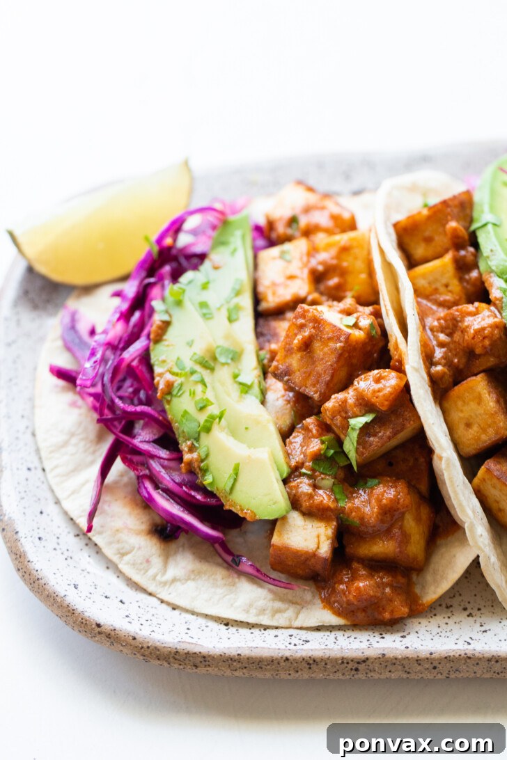 Flavor-Packed Sriracha Tofu Tacos 7 One vegan taco filled with Trader Joe's sriracha tofu on a ceramic plate, topped with avocado, red cabbage, salsa, and cilantro.